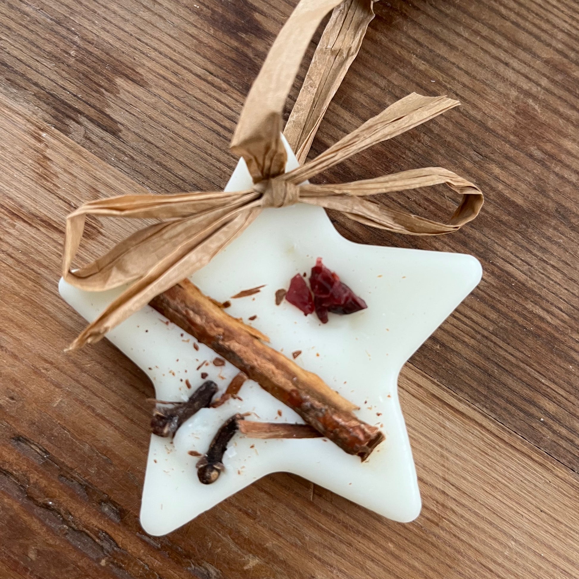 Star-shaped hanging wax melt with cinnamon sticks and dried berries on a wooden surface