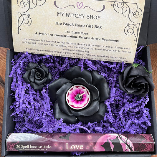 A black rose spell incense gift box from My Witchy Shop, featuring three black roses in purple shredded paper, with a central black rose containing a pink and white wax candle. A card explains the black rose symbolism, and a box of 20 spell incense sticks is visible at the bottom.