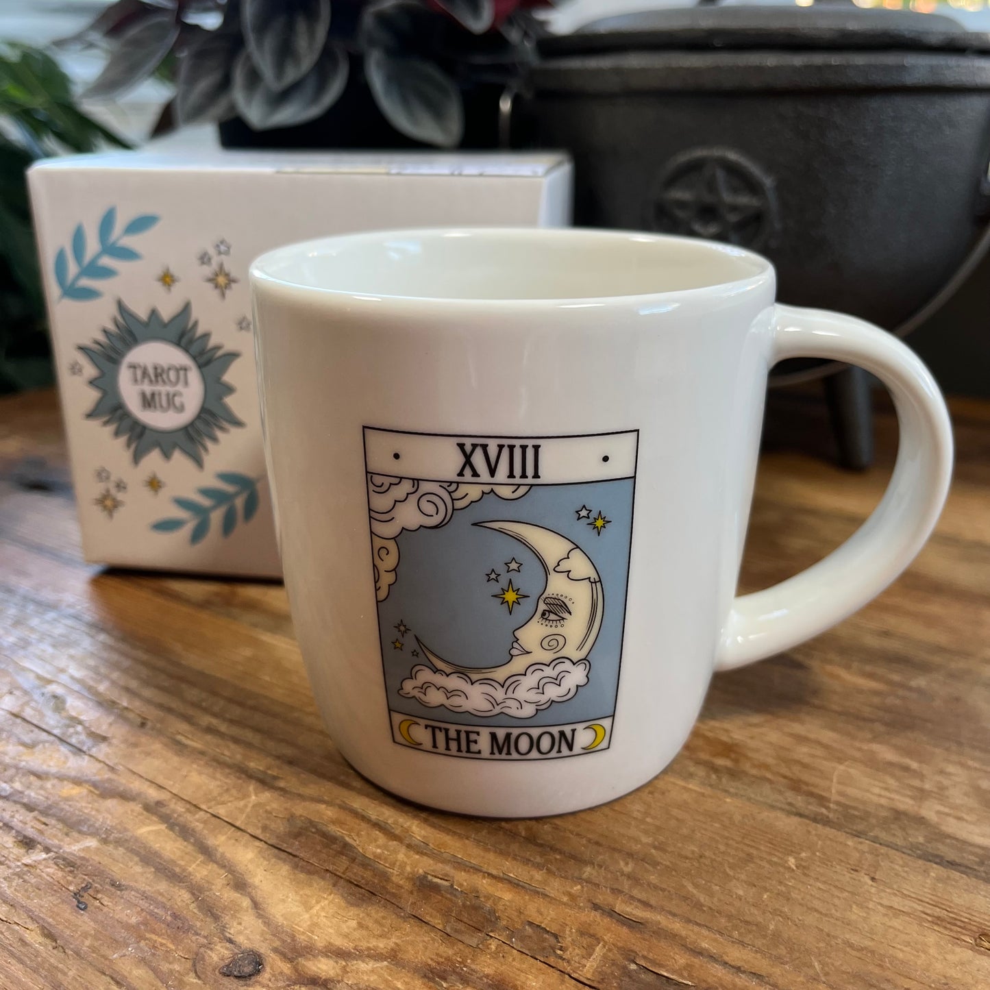 White mug with 'The Moon' tarot card design on a wooden surface, with a box labeled 'Tarot Mug' in the background.