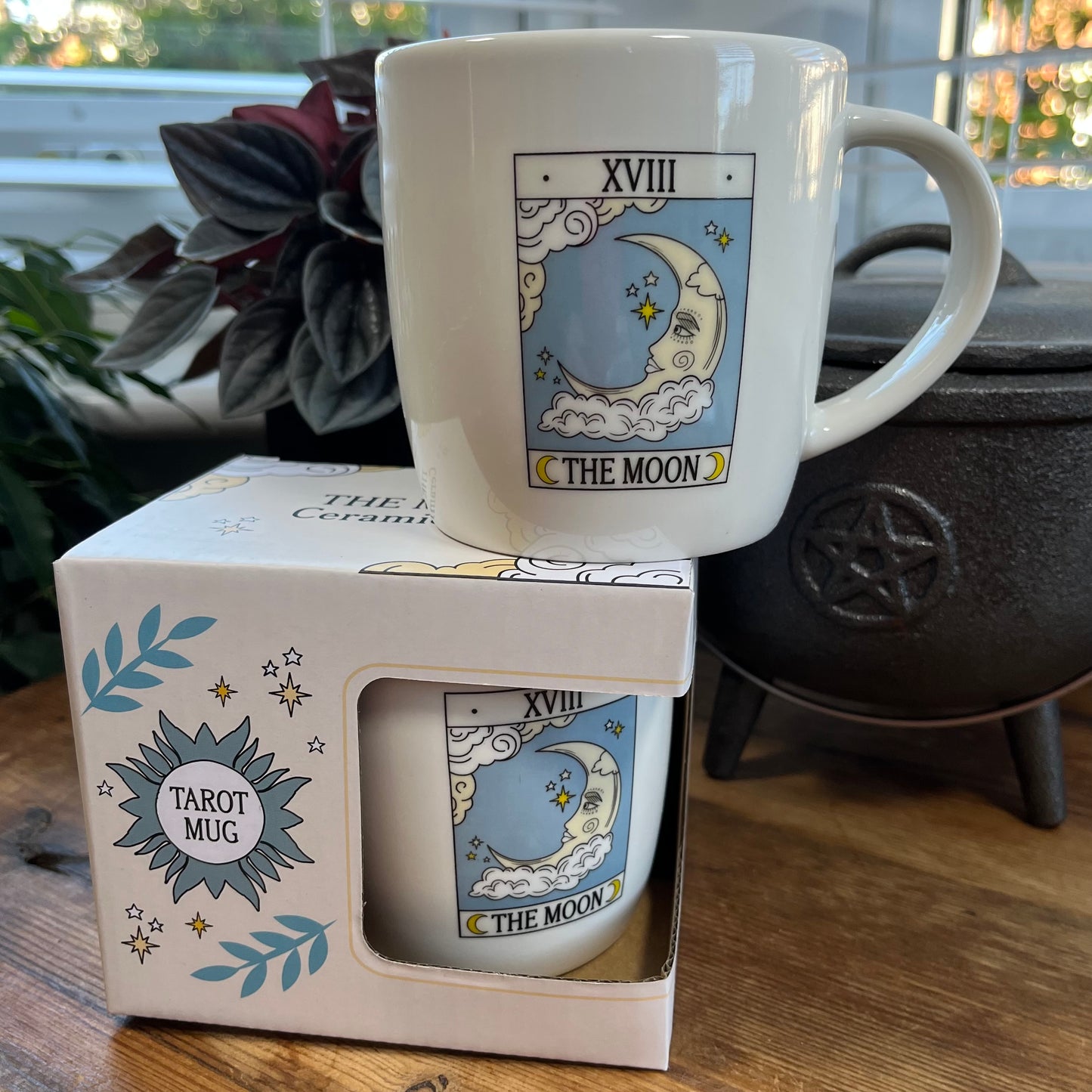 Mug with 'The Moon' tarot card design on a matching box, with plants and decor in the background.