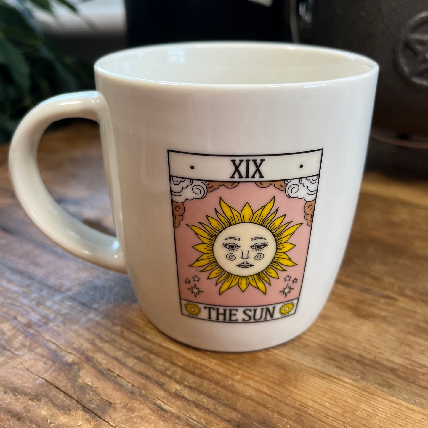 White mug with 'The Sun' tarot card design on a wooden surface