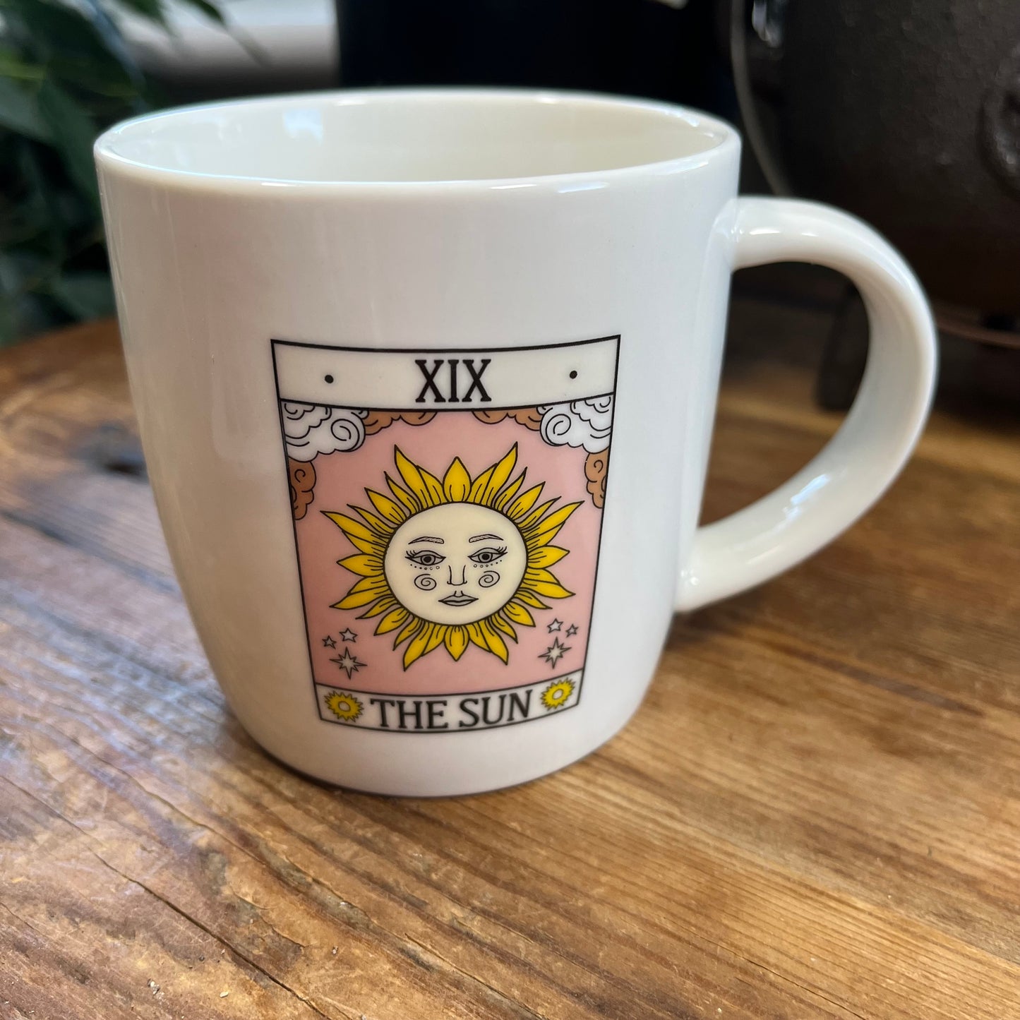 White mug with 'The Sun' tarot card design on a wooden surface