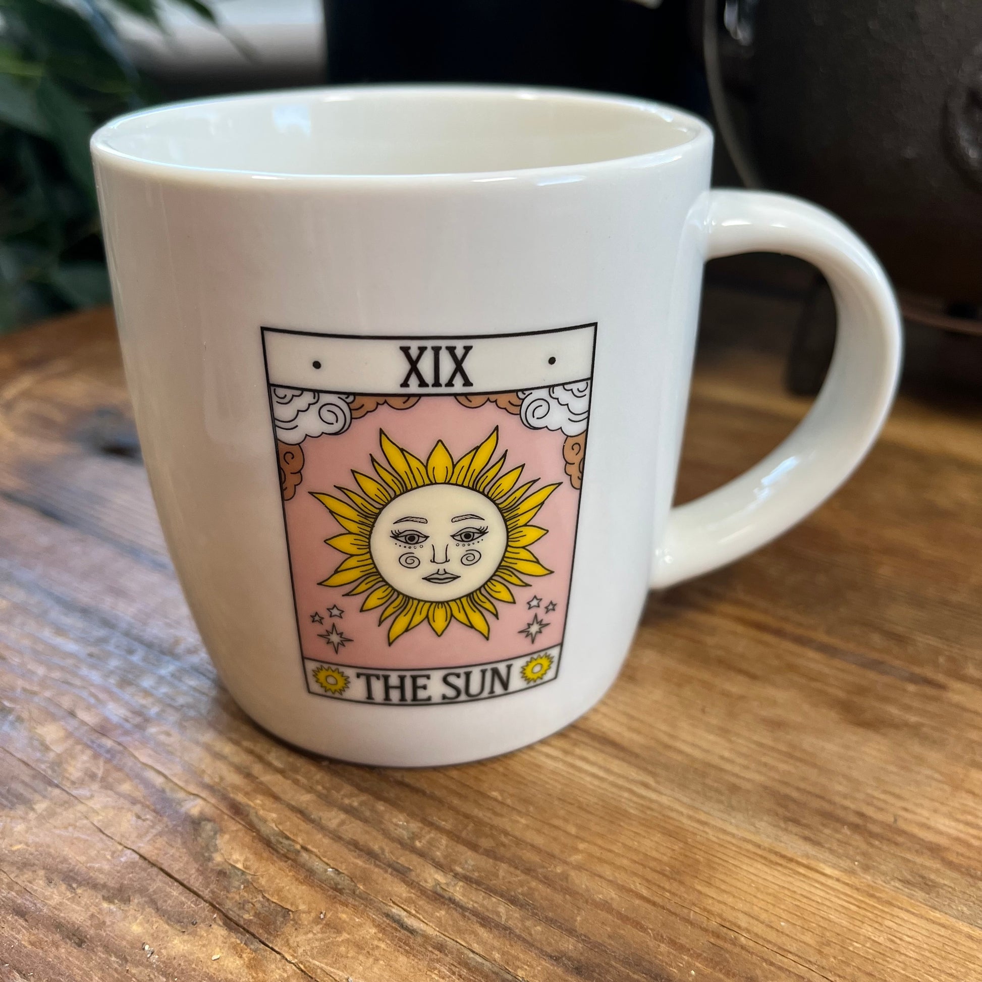 White mug with 'The Sun' tarot card design on a wooden surface