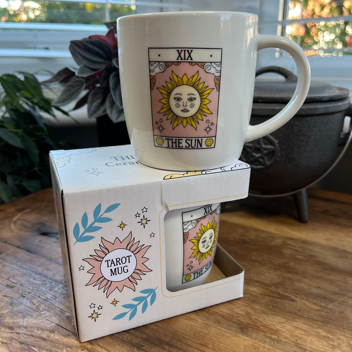 White mug with tarot design in a box on a wooden surface