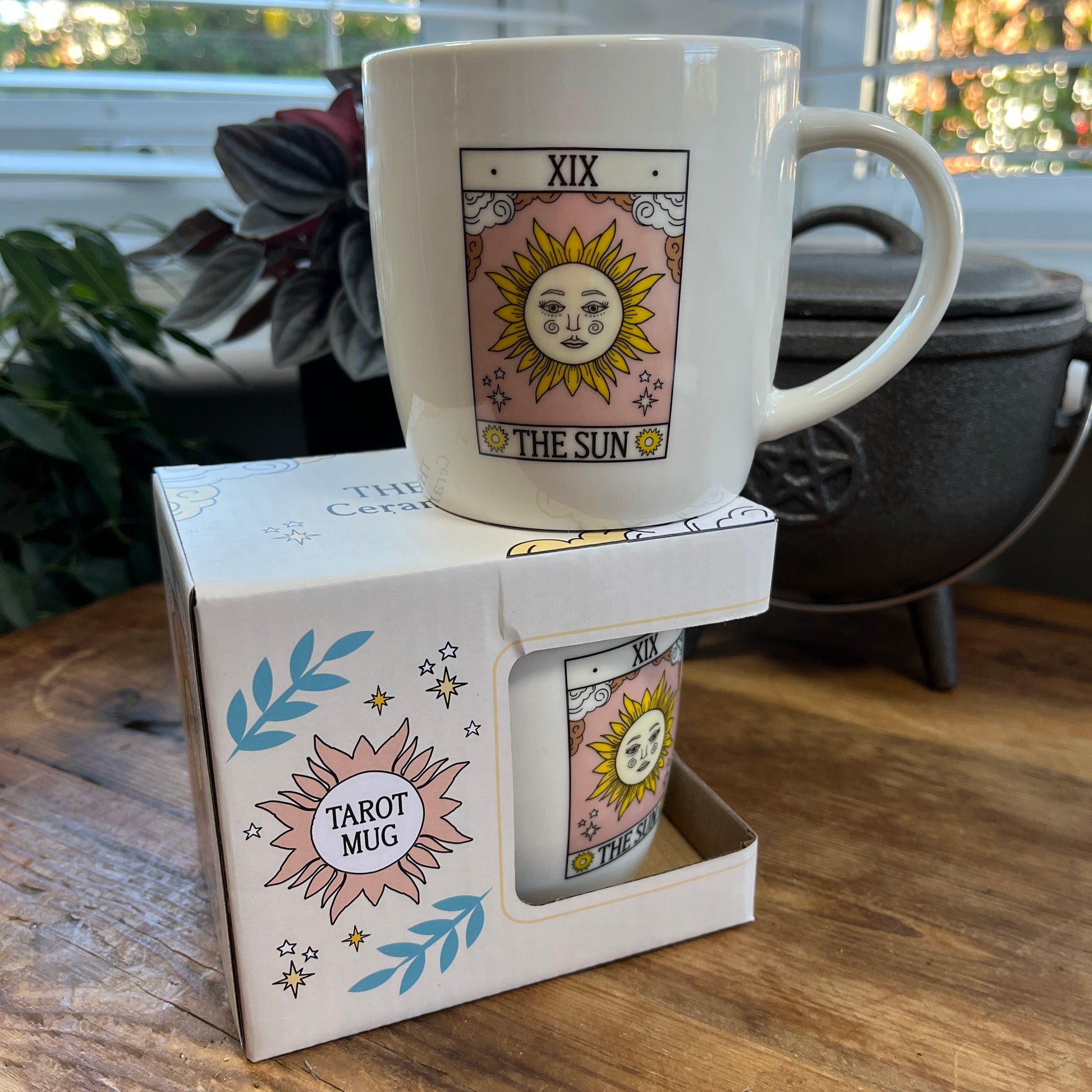 White mug with tarot design in a box on a wooden surface
