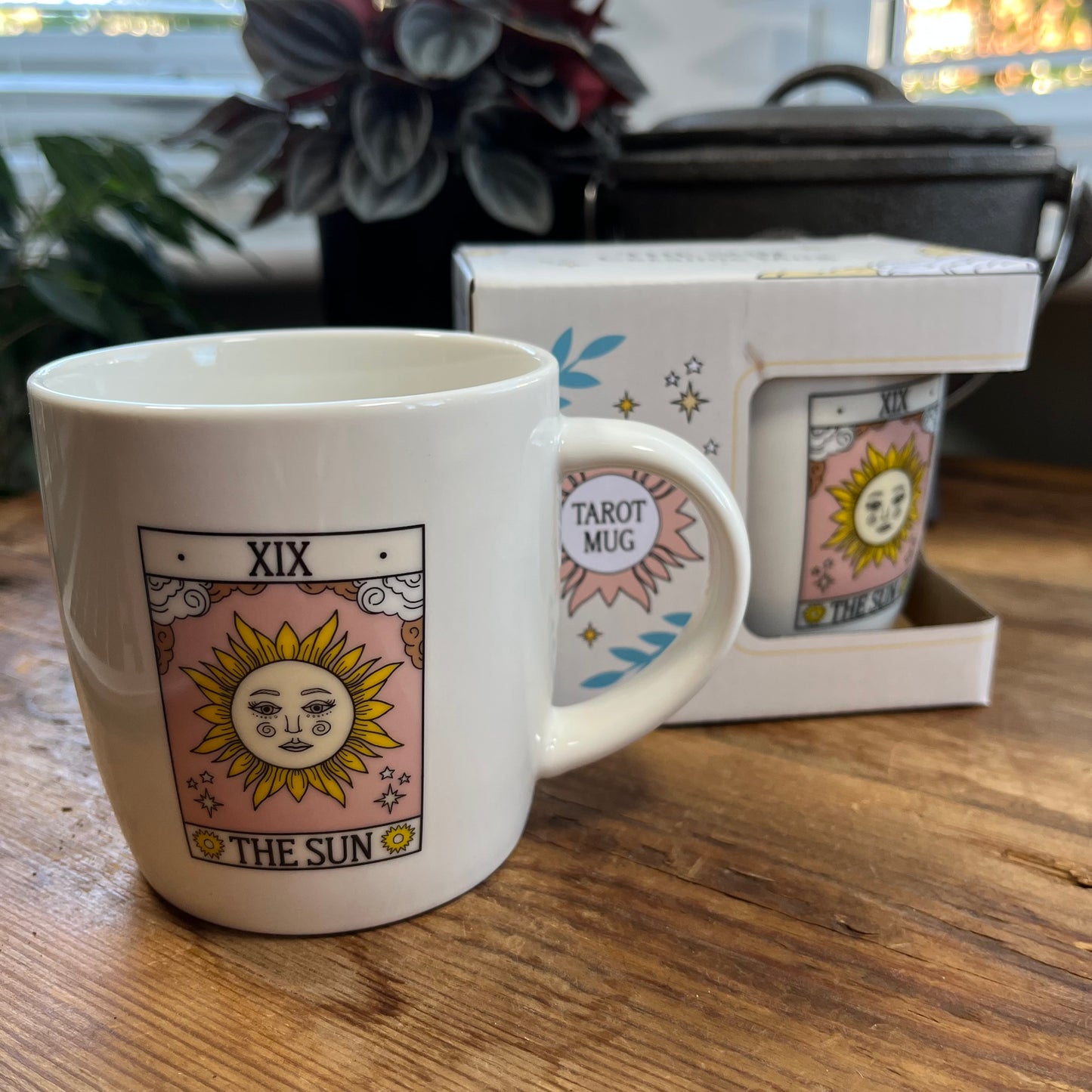 White mug with 'The Sun' design and tarot card elements on a wooden surface.