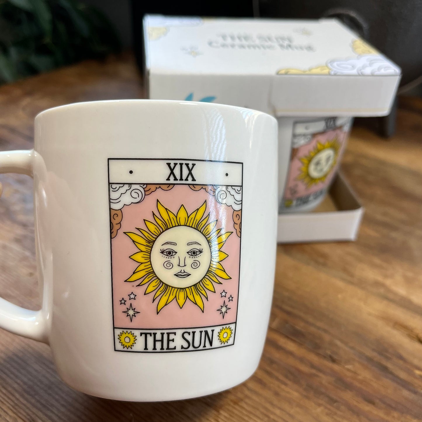 White mug with 'The Sun' tarot card design on a wooden surface