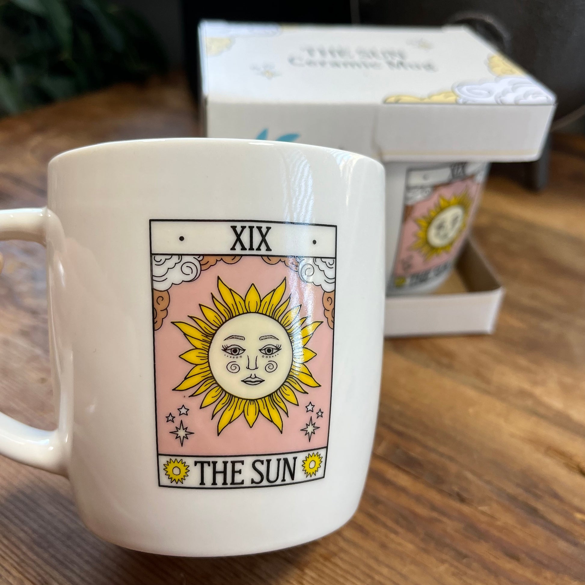 White mug with 'The Sun' tarot card design on a wooden surface