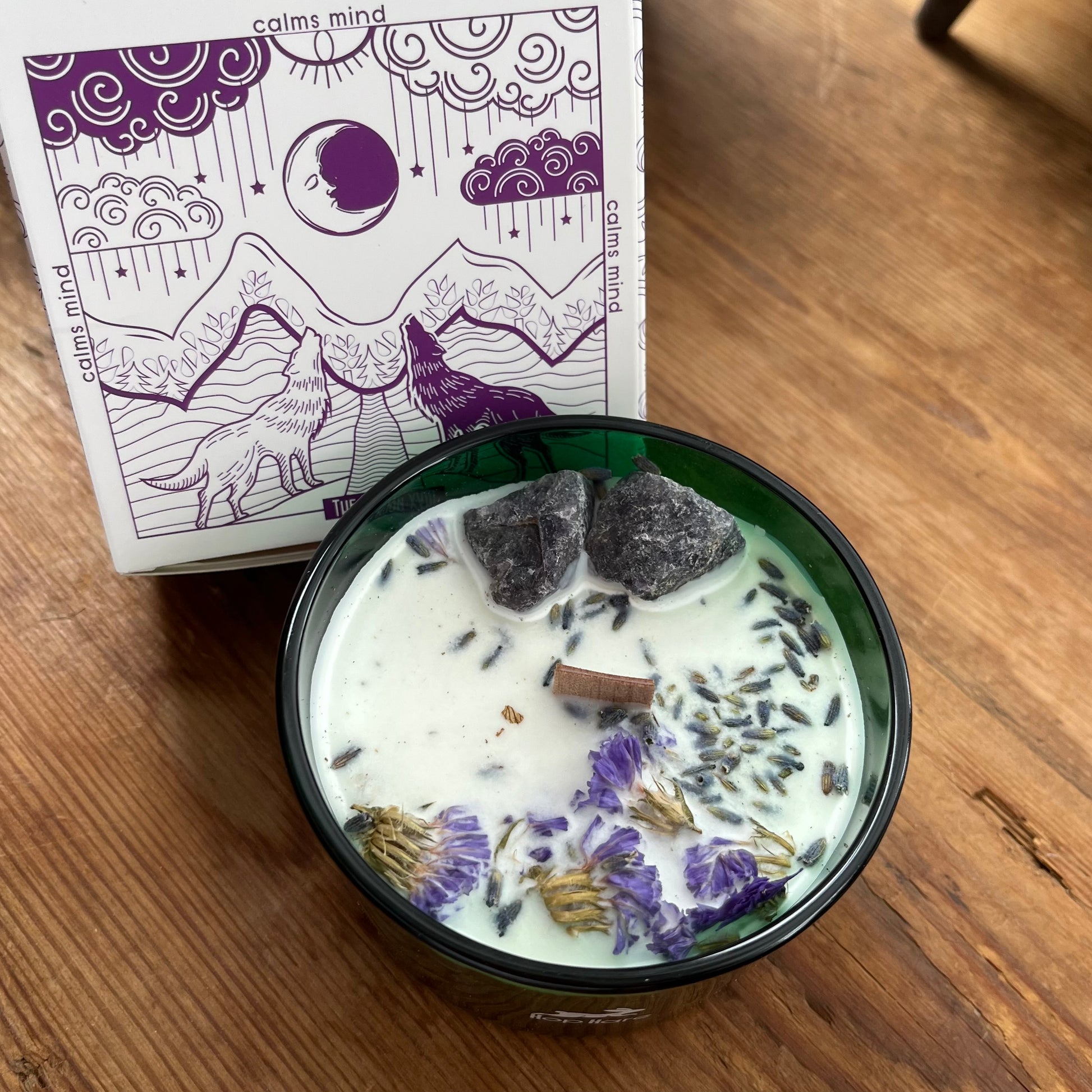 Candle decorated with flowers and crystals alongside moon tarot card 