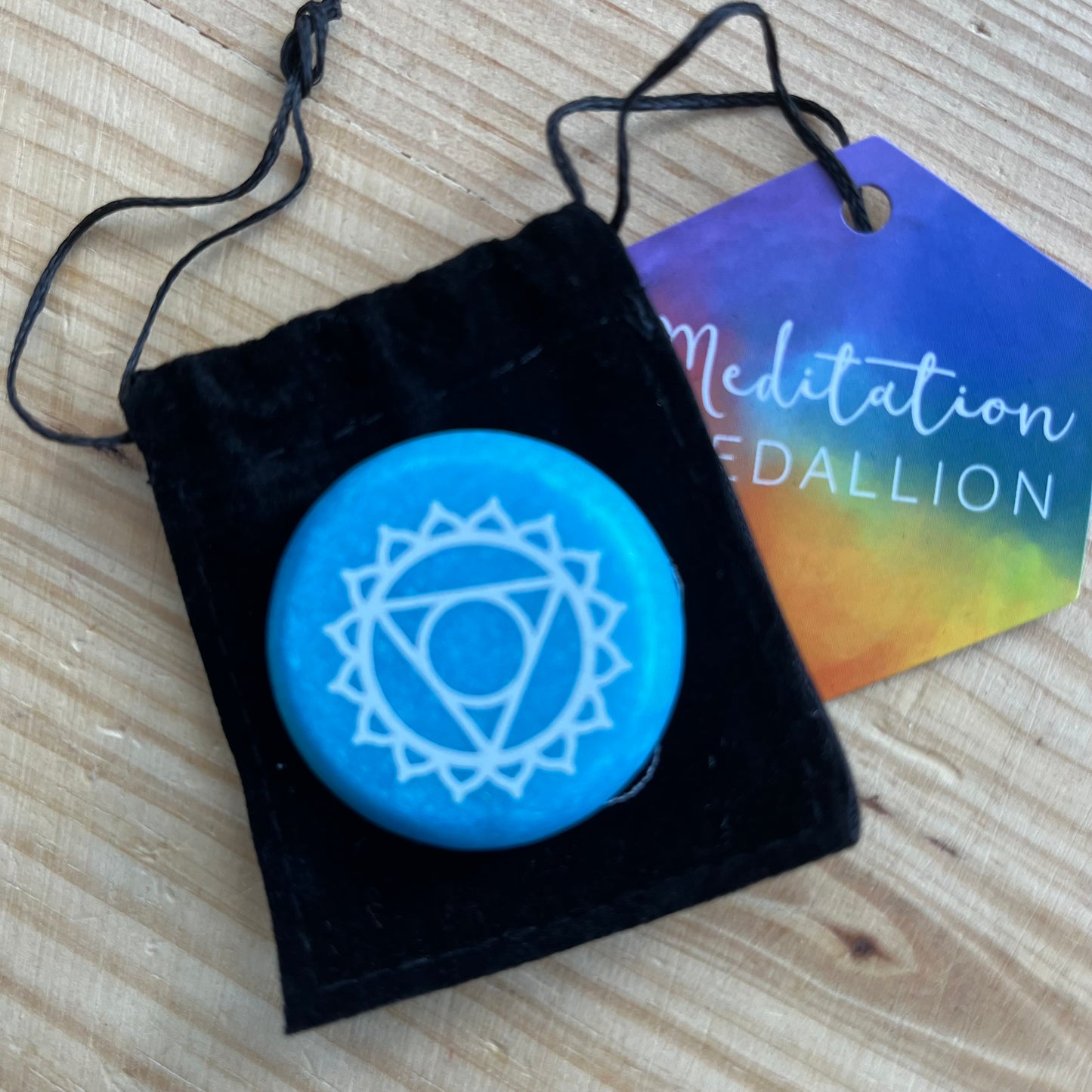 Blue flat circular meditation stone is engraved with the Throat Chakra symbol alongside it's black velvet pouch 
