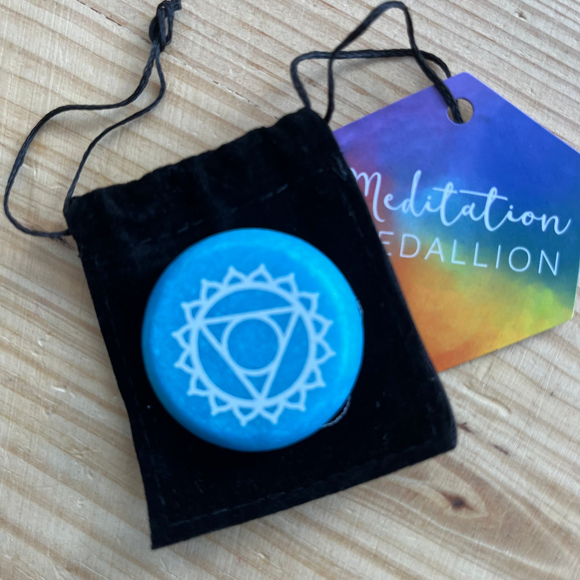 Blue flat circular meditation stone is engraved with the Throat Chakra symbol alongside it's black velvet pouch 
