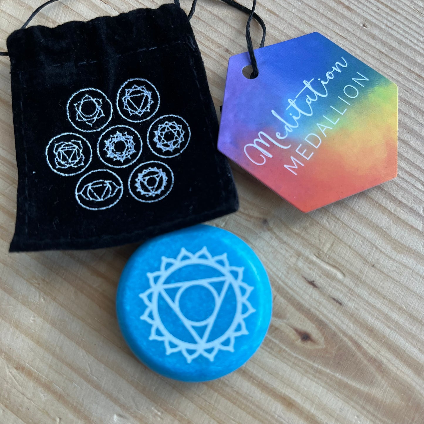 Blue flat circular meditation stone is engraved with the Throat Chakra symbol alongside it's black velvet pouch printed with the 7 Chakra symbols 