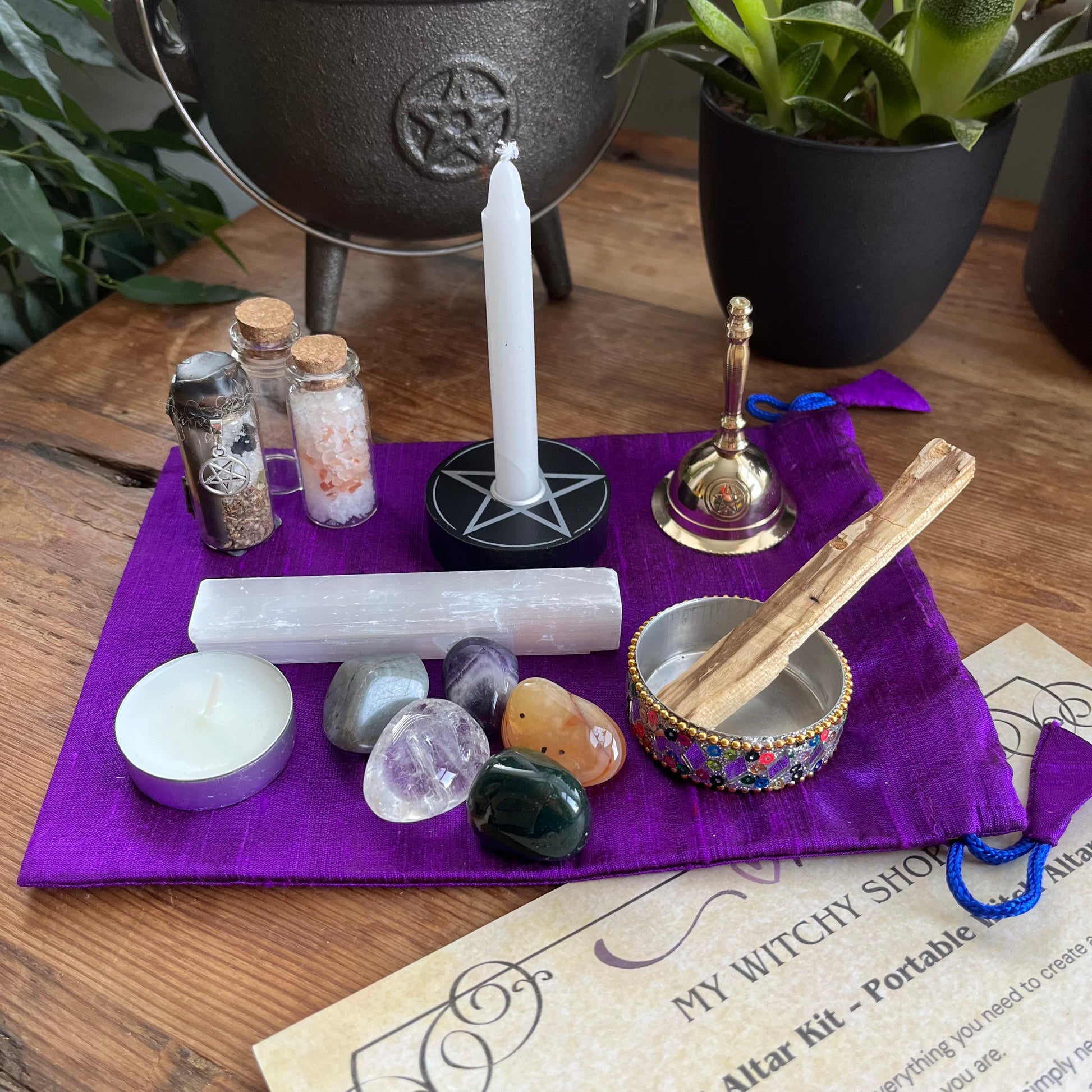 Witchy shop altar kit with candles, stones, and other items on a purple cloth.