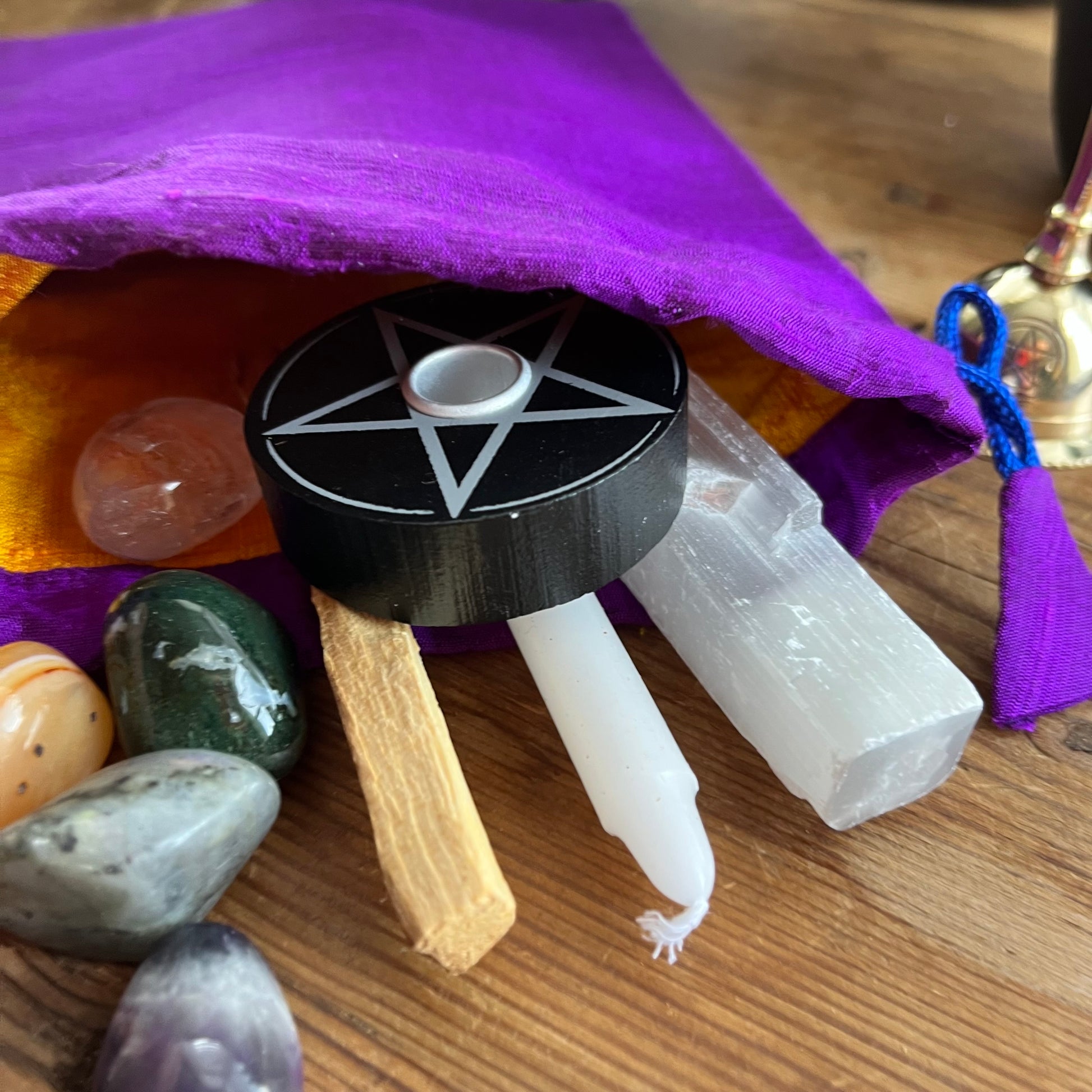 Wiccan or spiritual items including a pentacle candle holder, stones, and a crystal on a wooden surface with a purple cloth.