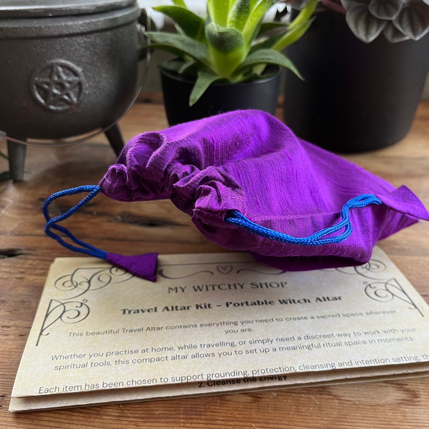 Purple drawstring bag on a wooden surface with a card about a travel altar kit.