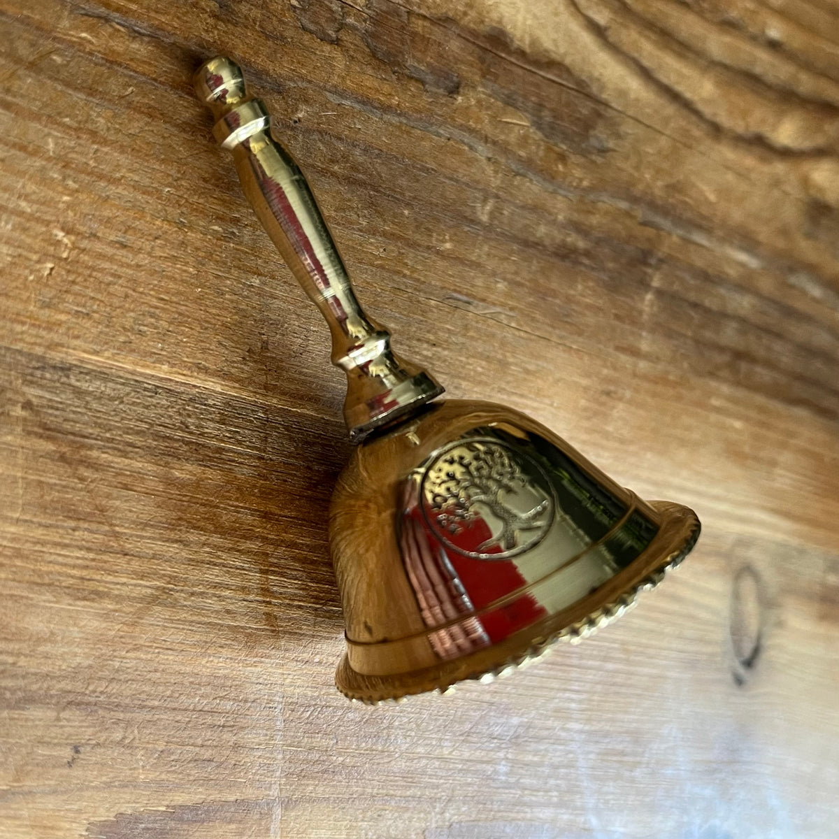 A  brass bell with a decorative handle, lying on a rustic wooden surface.