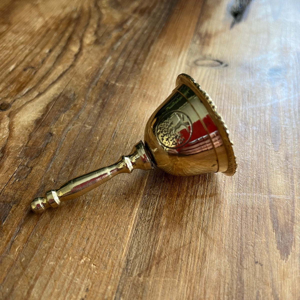 A small brass bell with a decorative handle, lying on a rustic wooden surface.