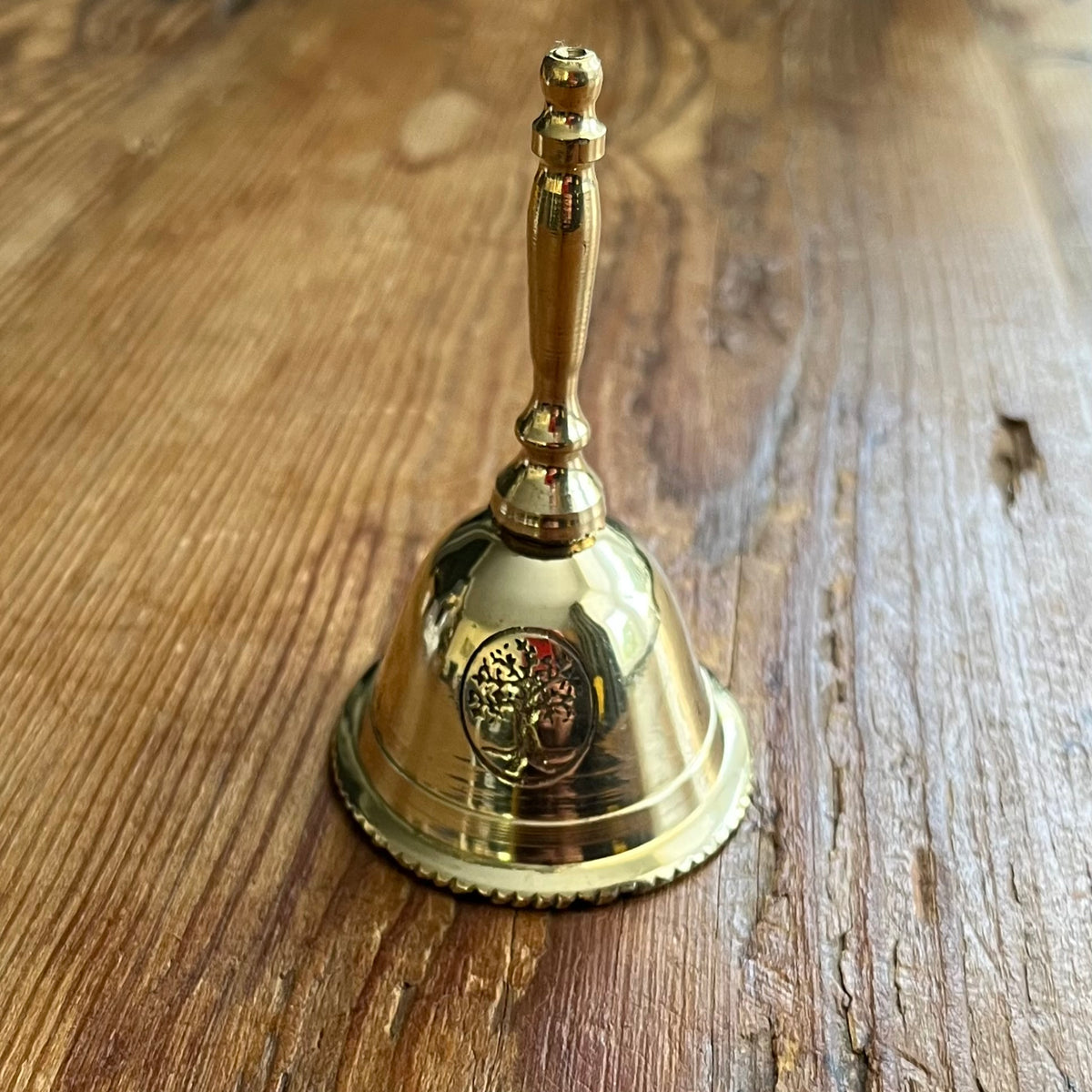 A polished brass bell with a decorative handle and a circular emblem on the front, resting on a rustic wooden surface.