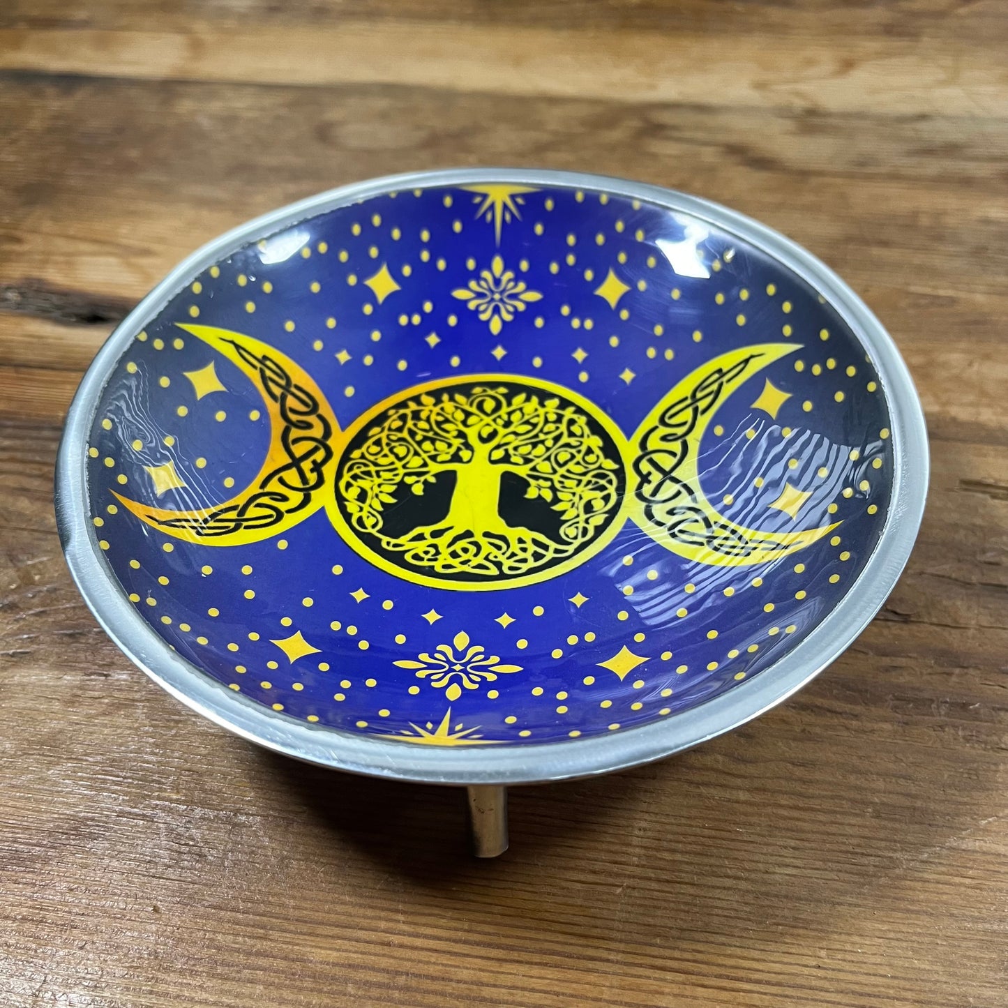 Decorative plate with yellow tree design and moon phases on a blue background, placed on a wooden surface.