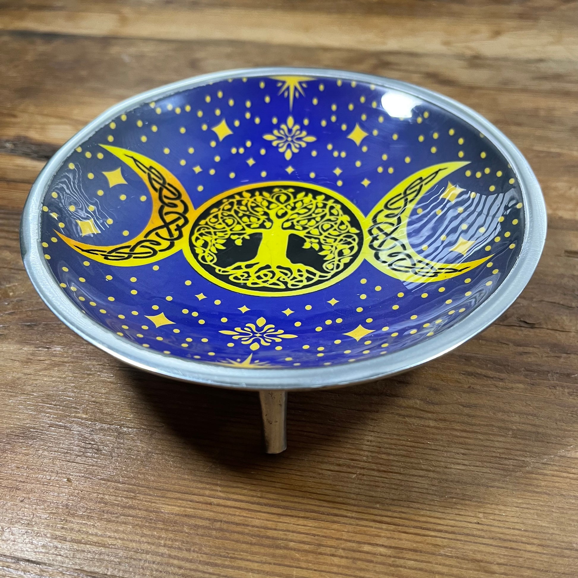 Decorative plate with yellow tree of life and moon designs on a blue background, placed on a wooden surface.