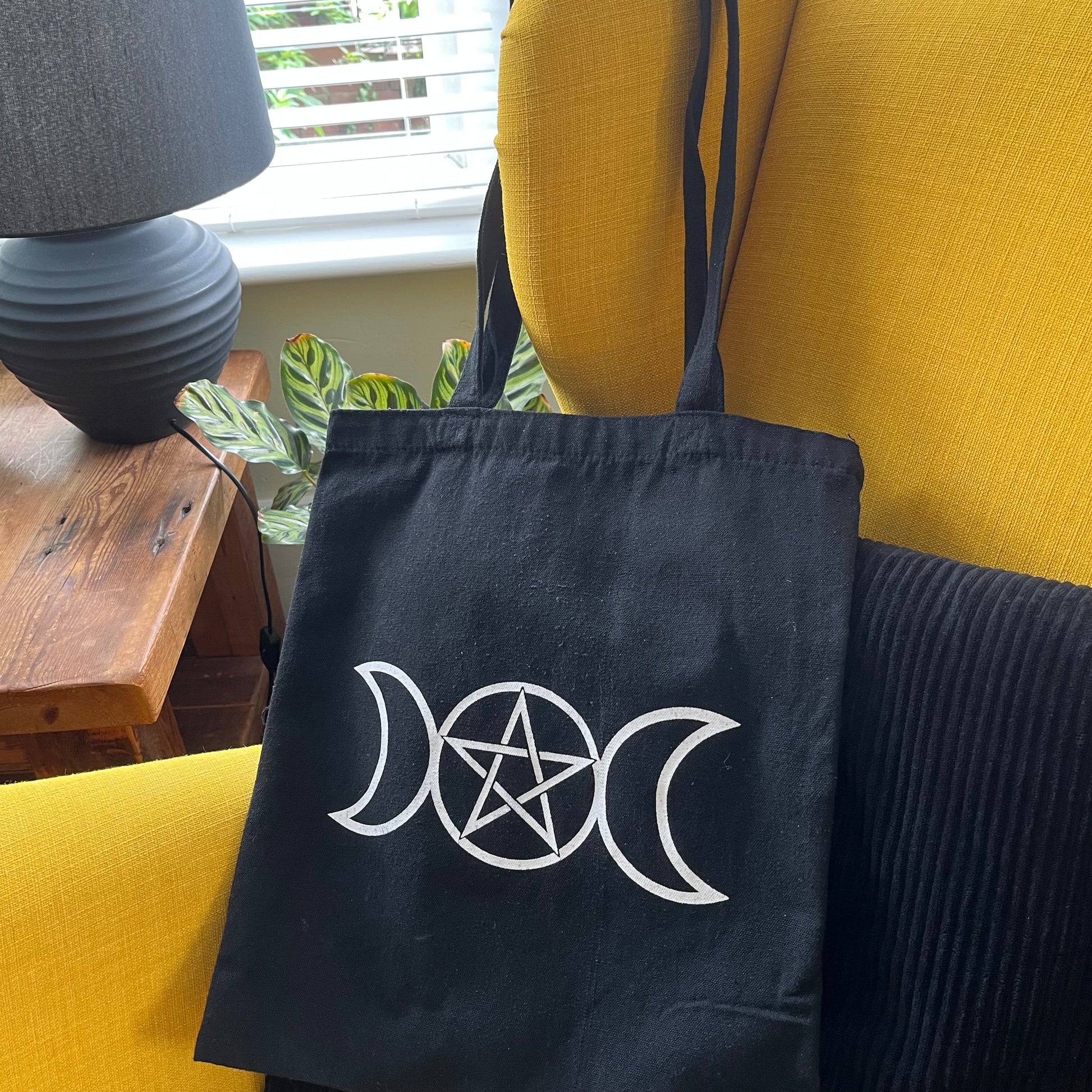 Black tote bag with white symbol on a yellow couch
