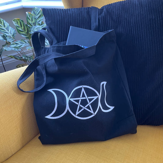 Black bag with white triple moon and pentagram symbol on a yellow couch