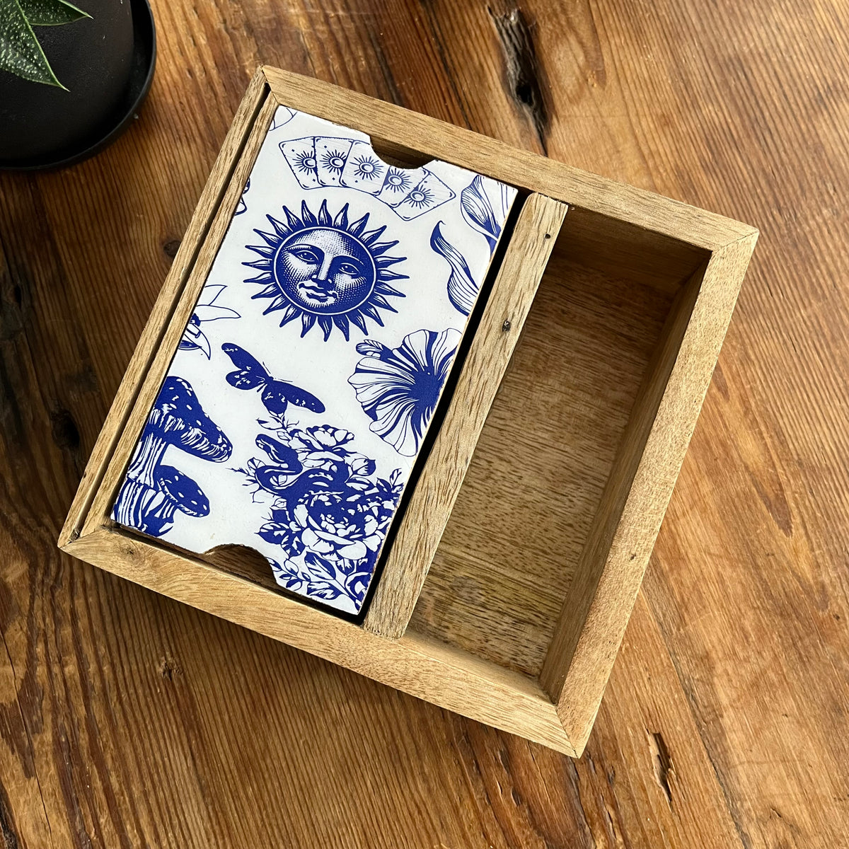 A wooden storage box for Tarot or Oracle cards with a blue and white celestial pattern, presented ion a wooden tabletop.