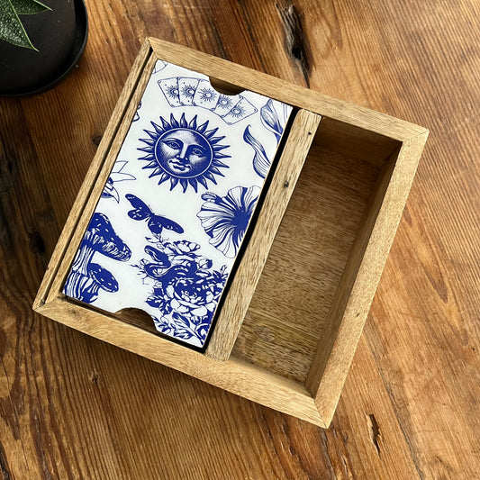 A wooden storage box for Tarot or Oracle cards with a blue and white celestial pattern, presented ion a wooden tabletop.