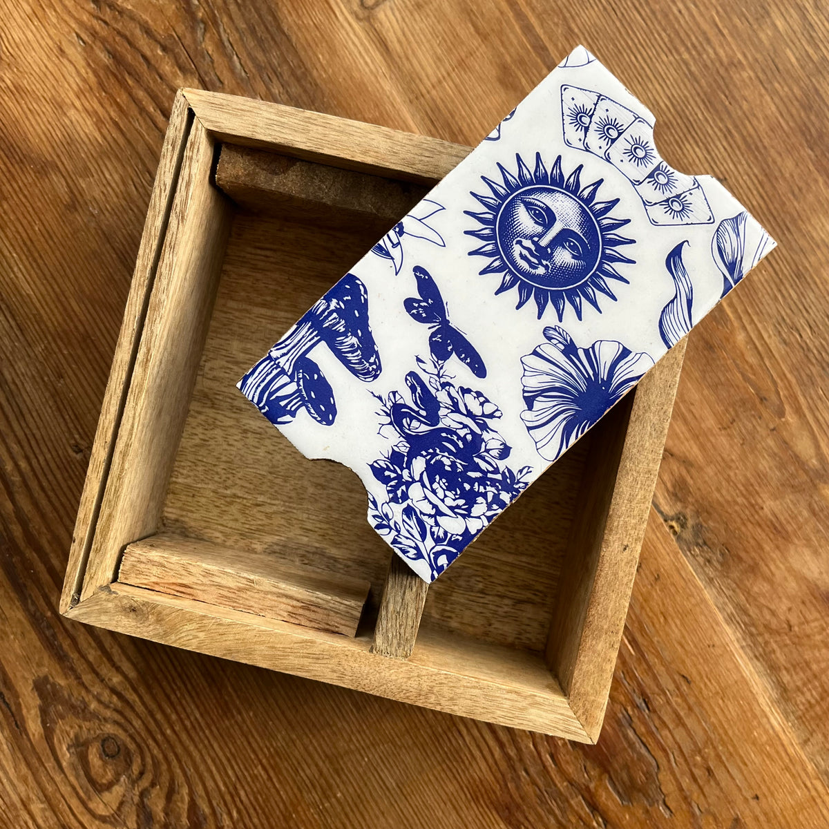 A wooden Tarot or Oracle card storage box with a blue floral and celestial print, resting on a wooden tabletop.