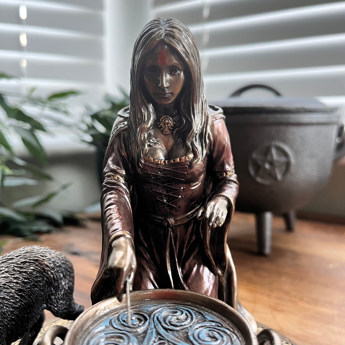 A bronze-finished witch figurine depicted with a cauldron 