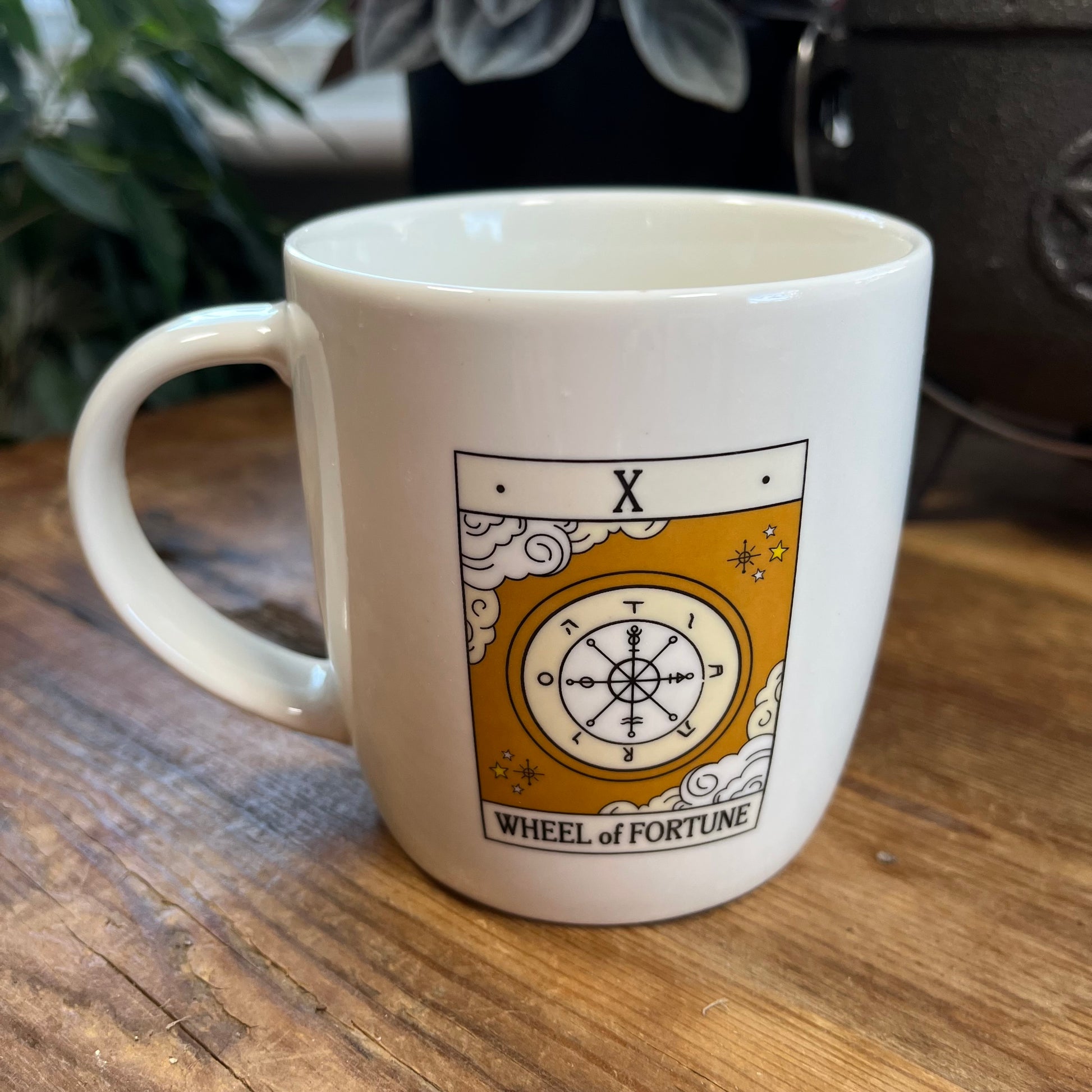 White mug with 'Wheel of Fortune' tarot design on a wooden surface