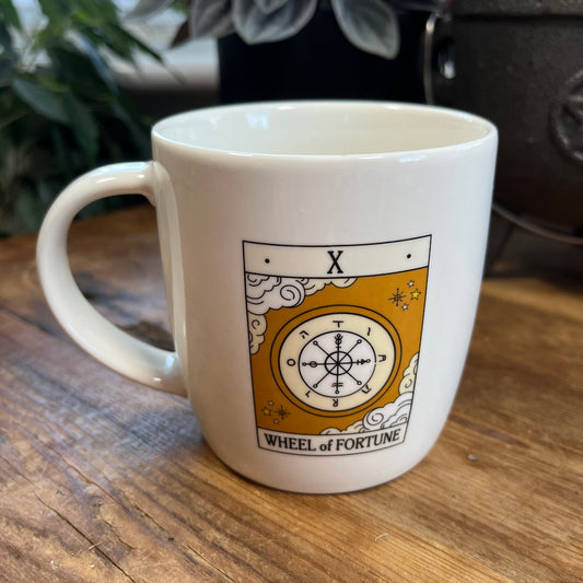 White mug with 'Wheel of Fortune' tarot design on a wooden surface