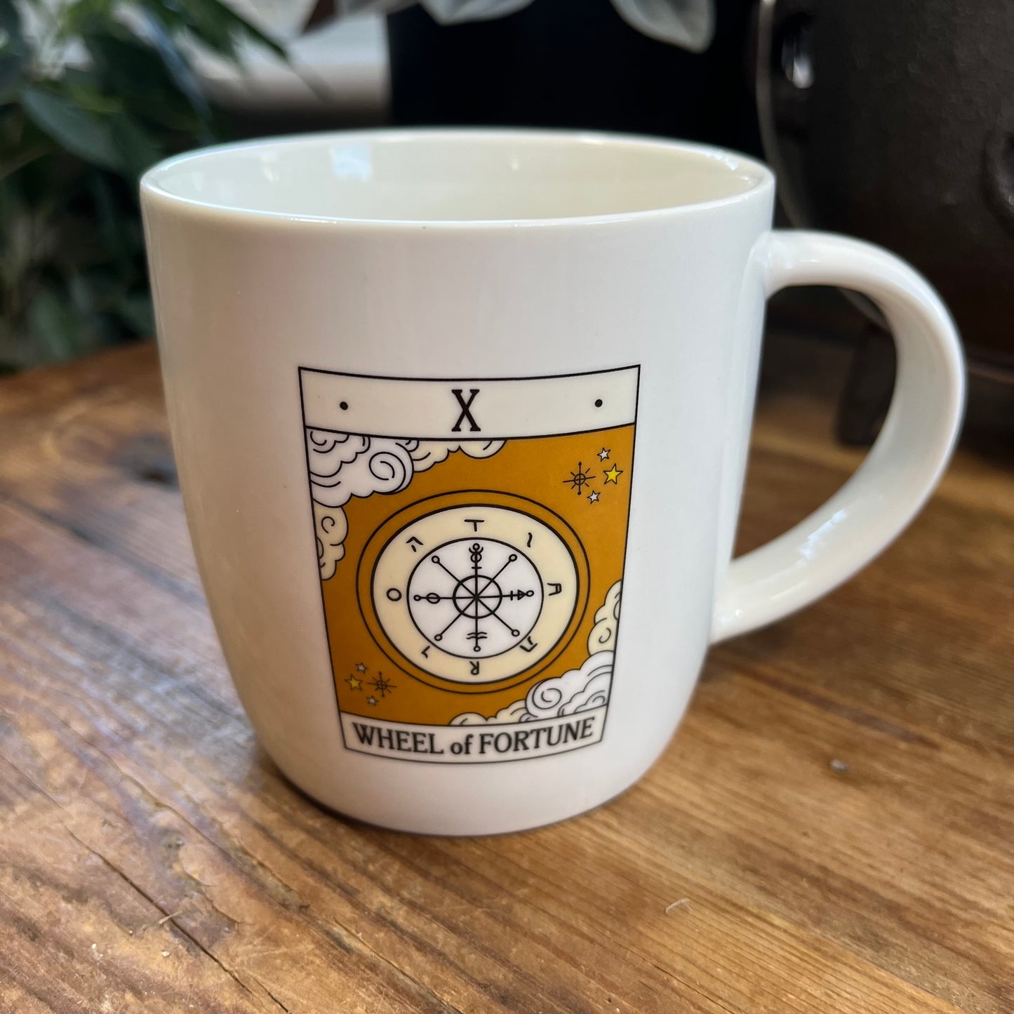 White mug with 'Wheel of Fortune' tarot design on a wooden surface
