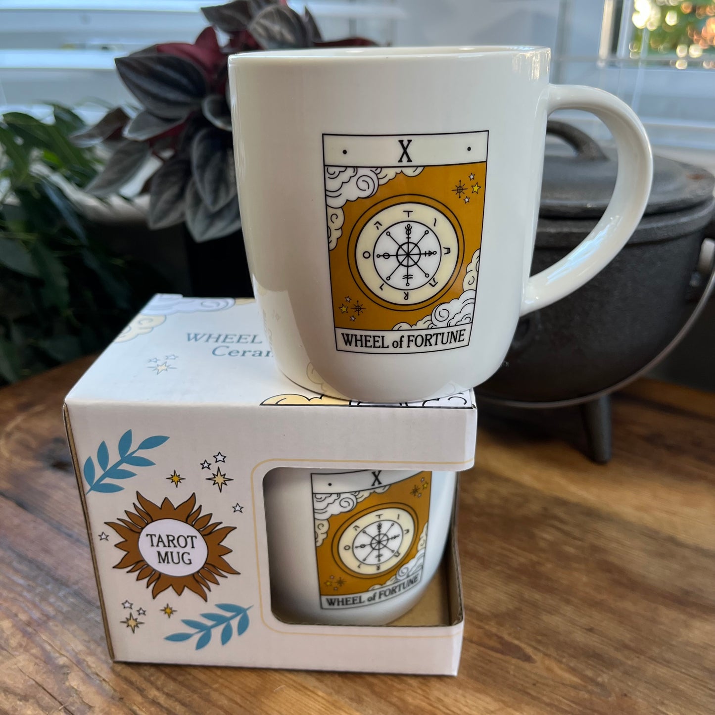 White mug with 'Wheel of Fortune' tarot design on a matching box, placed on a wooden surface.