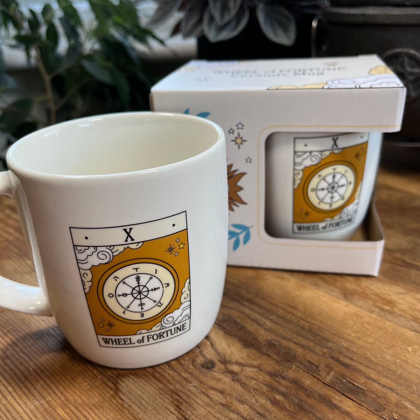 Mug with 'Wheel of Fortune' tarot design in front of a matching box on a wooden surface.
