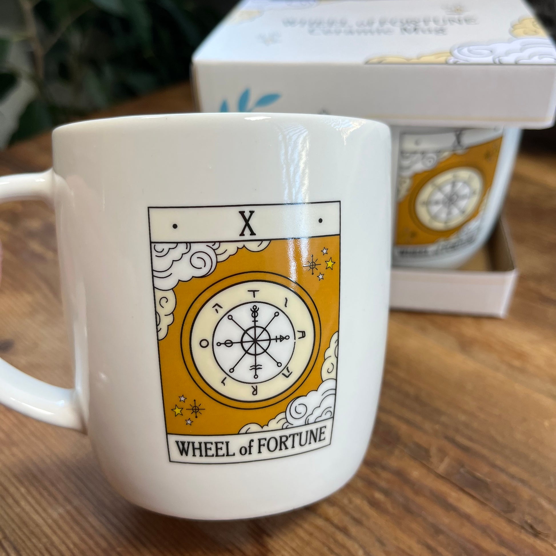 White mug with 'Wheel of Fortune' tarot design on a wooden surface