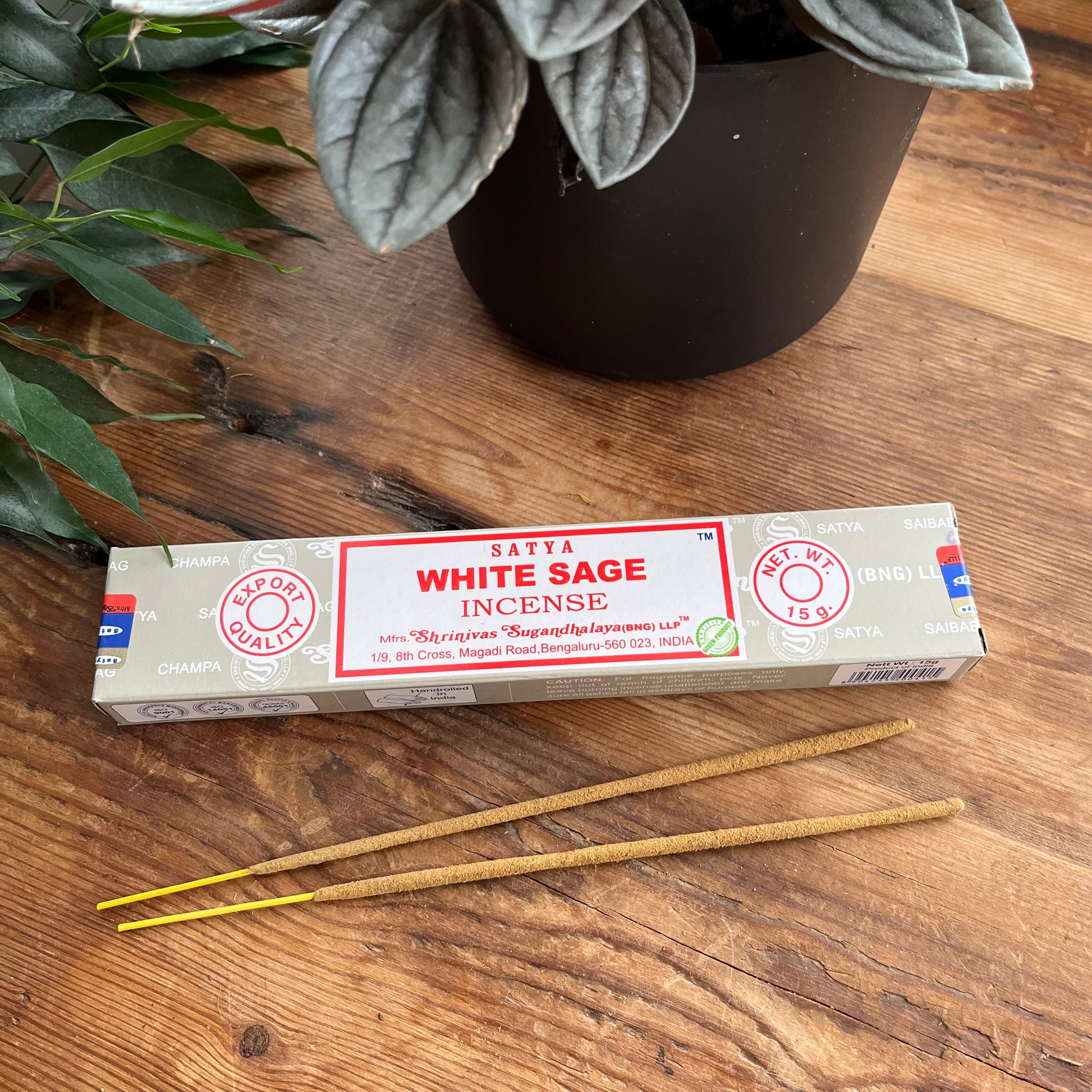 Box of Satya White Sage incense on a wooden surface with plants in the background