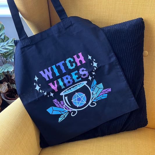 Black tote bag with 'Witch Vibes' design on a yellow couch