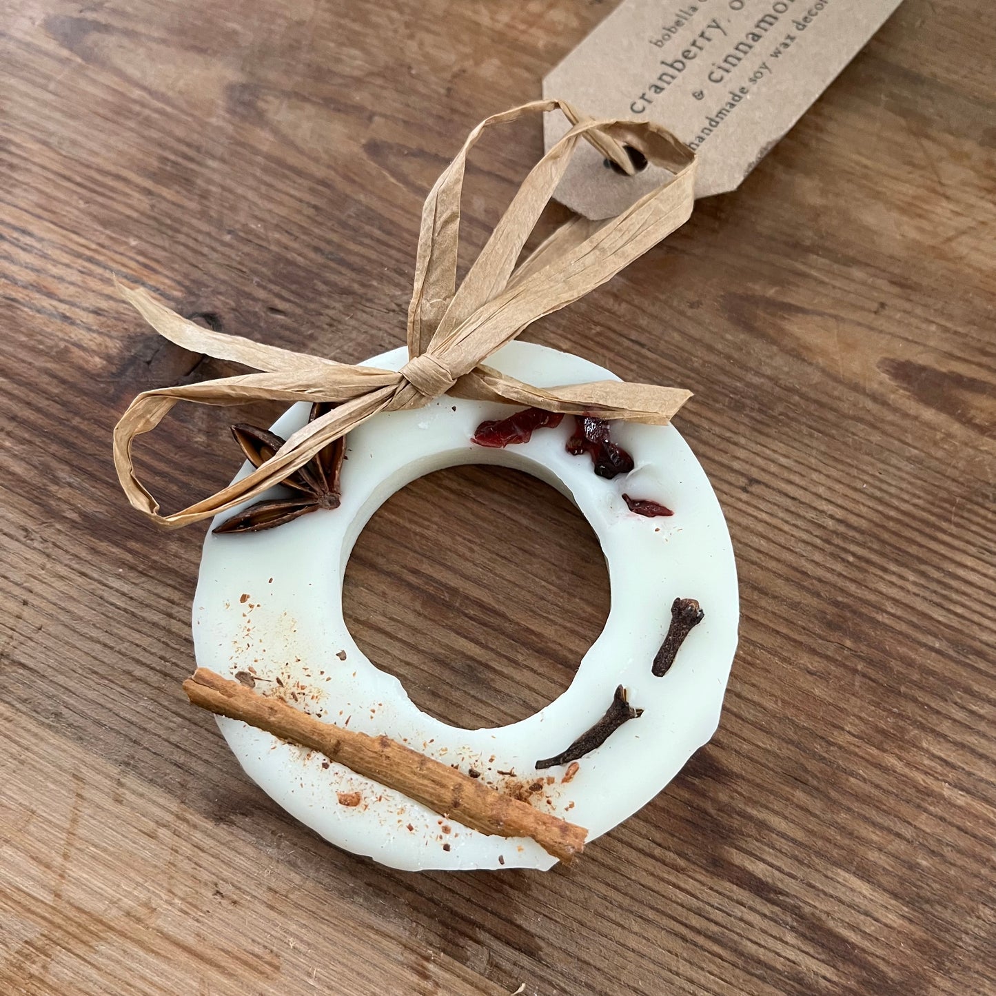 Decorative ring with cinnamon stick, star anise, and cardamom on a wooden surface with a tag.