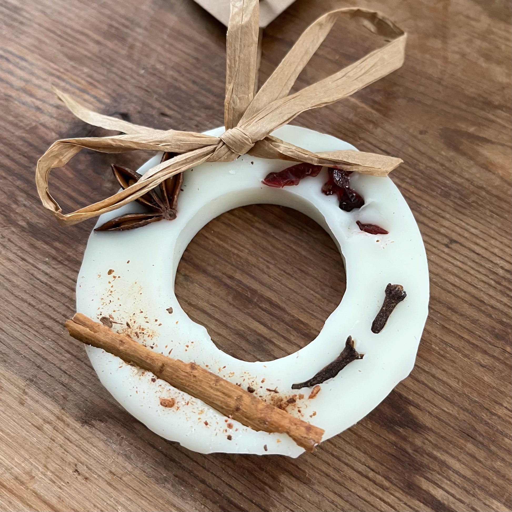 White wreath-shaped ornament with cinnamon stick and star anise on a wooden surface
