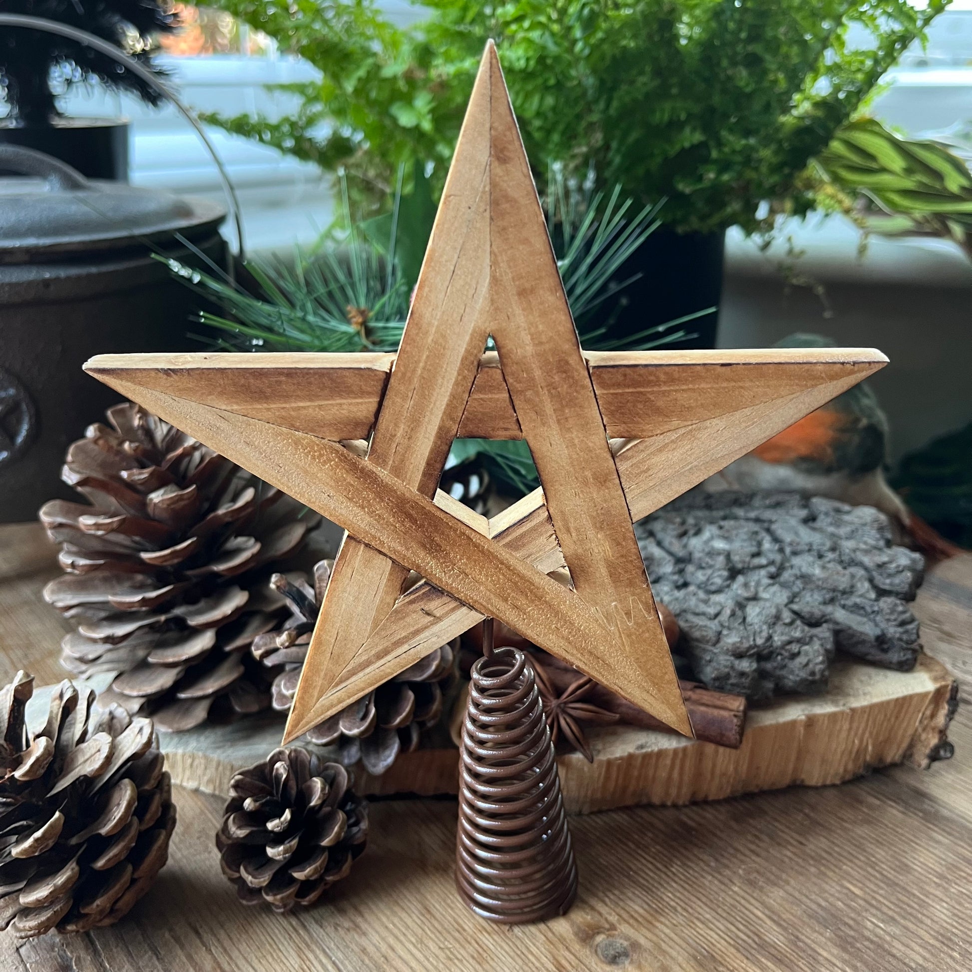 natural wooden Tree Topper in the shape of a pentagram star, shown with traditional christmas decorations of pine cones, holly and robin in the background 