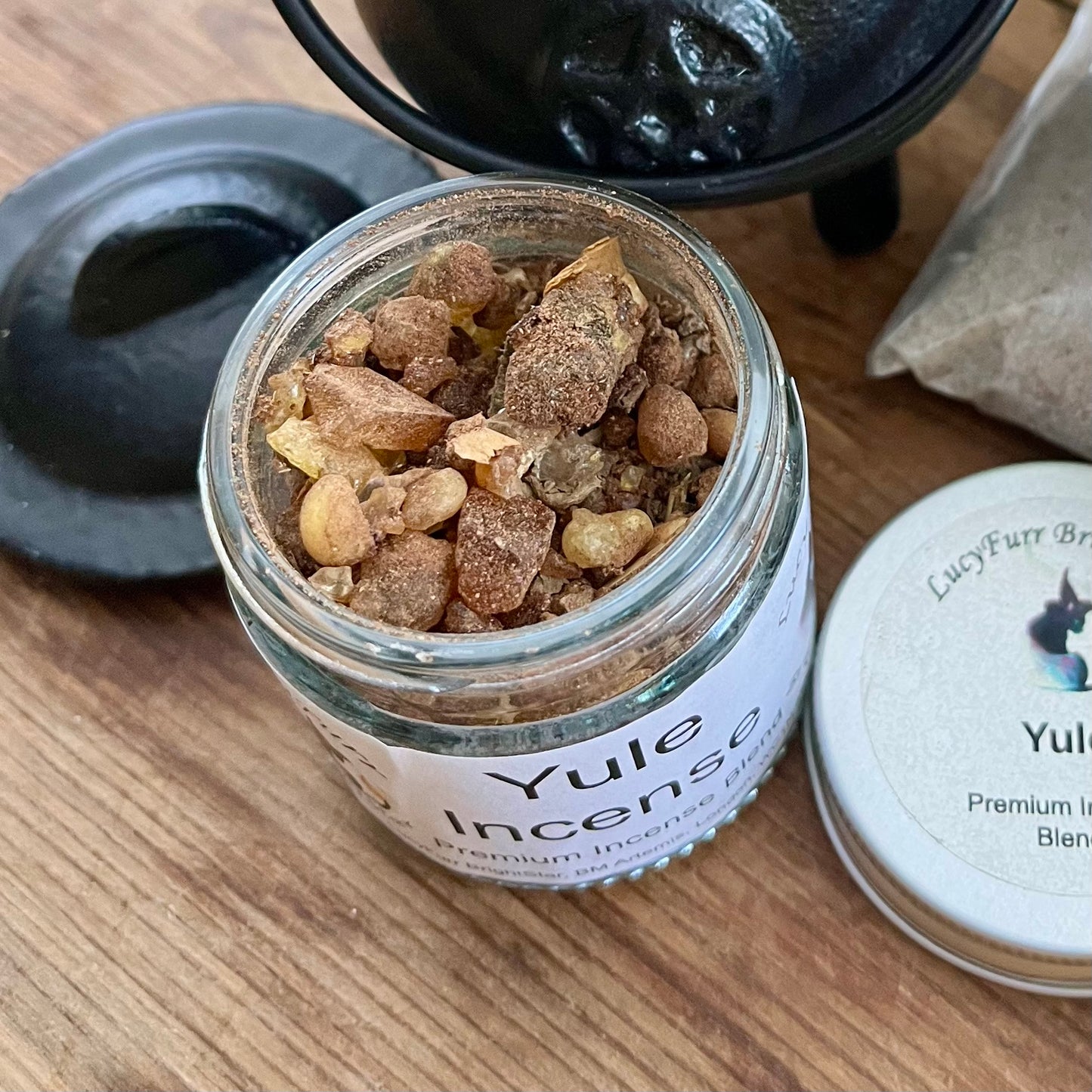 Jar of Yule Incense with a black coauldron and packaging on a wooden surface
