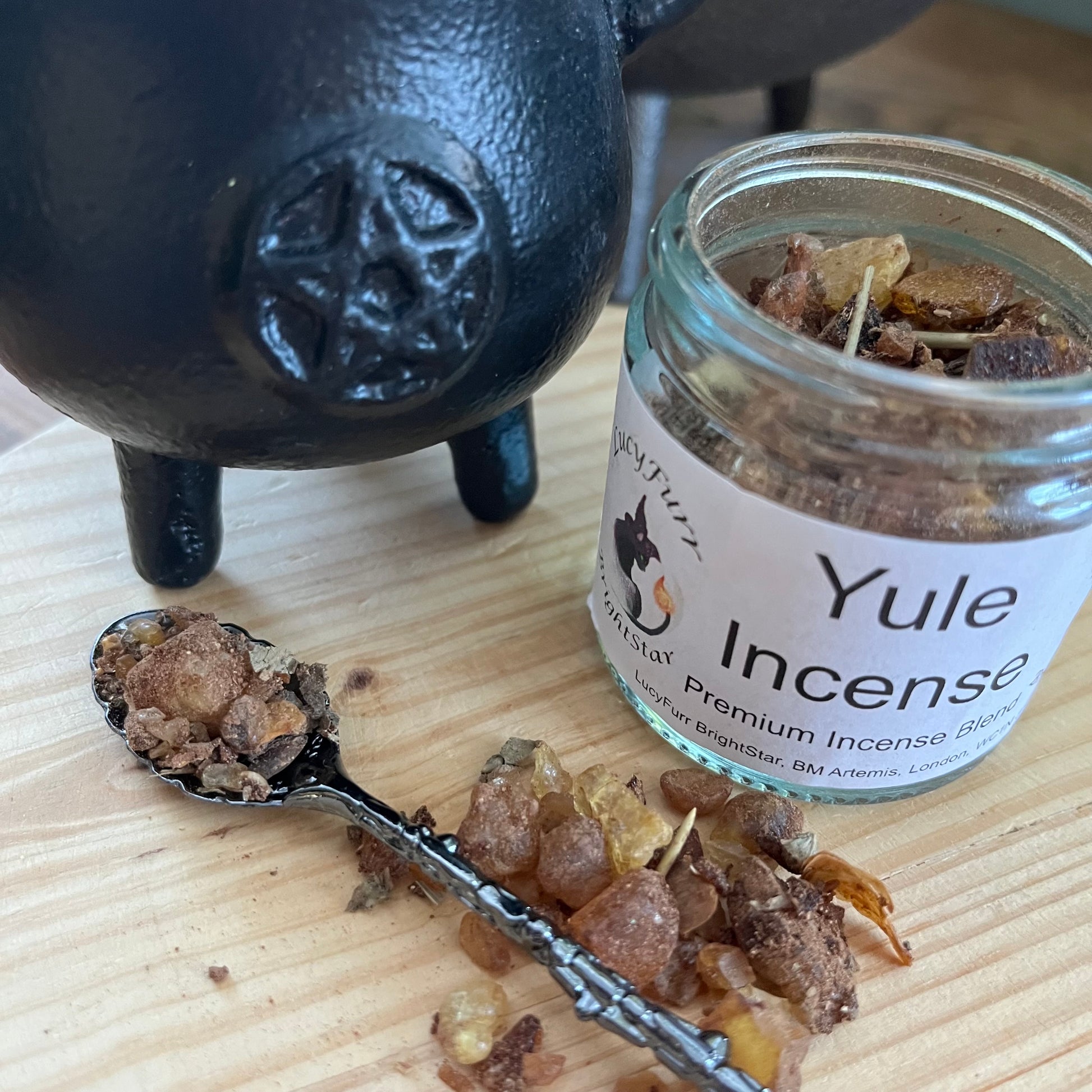 Yule Incense jar with incense on a spoon and black cauldron on a wooden surface