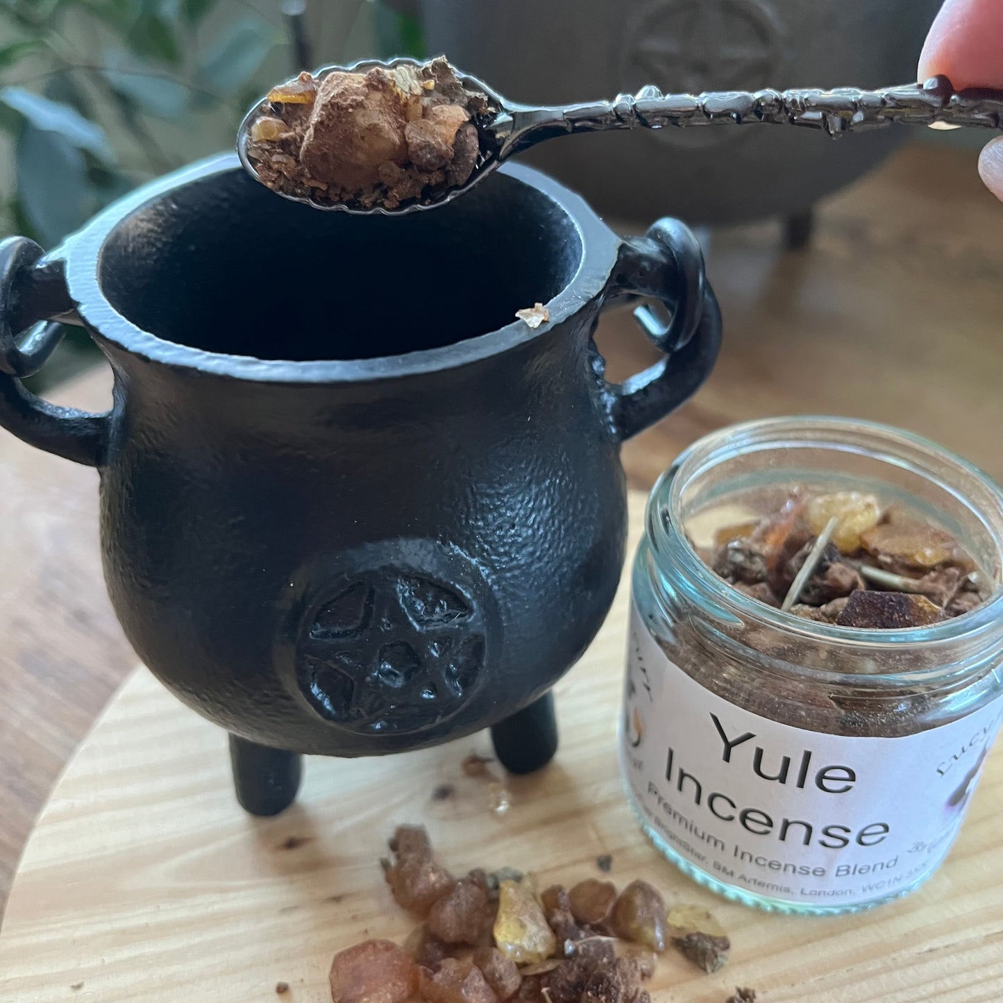 Black cauldron with Yule Incense jar and spoonful of incense on a wooden surface
