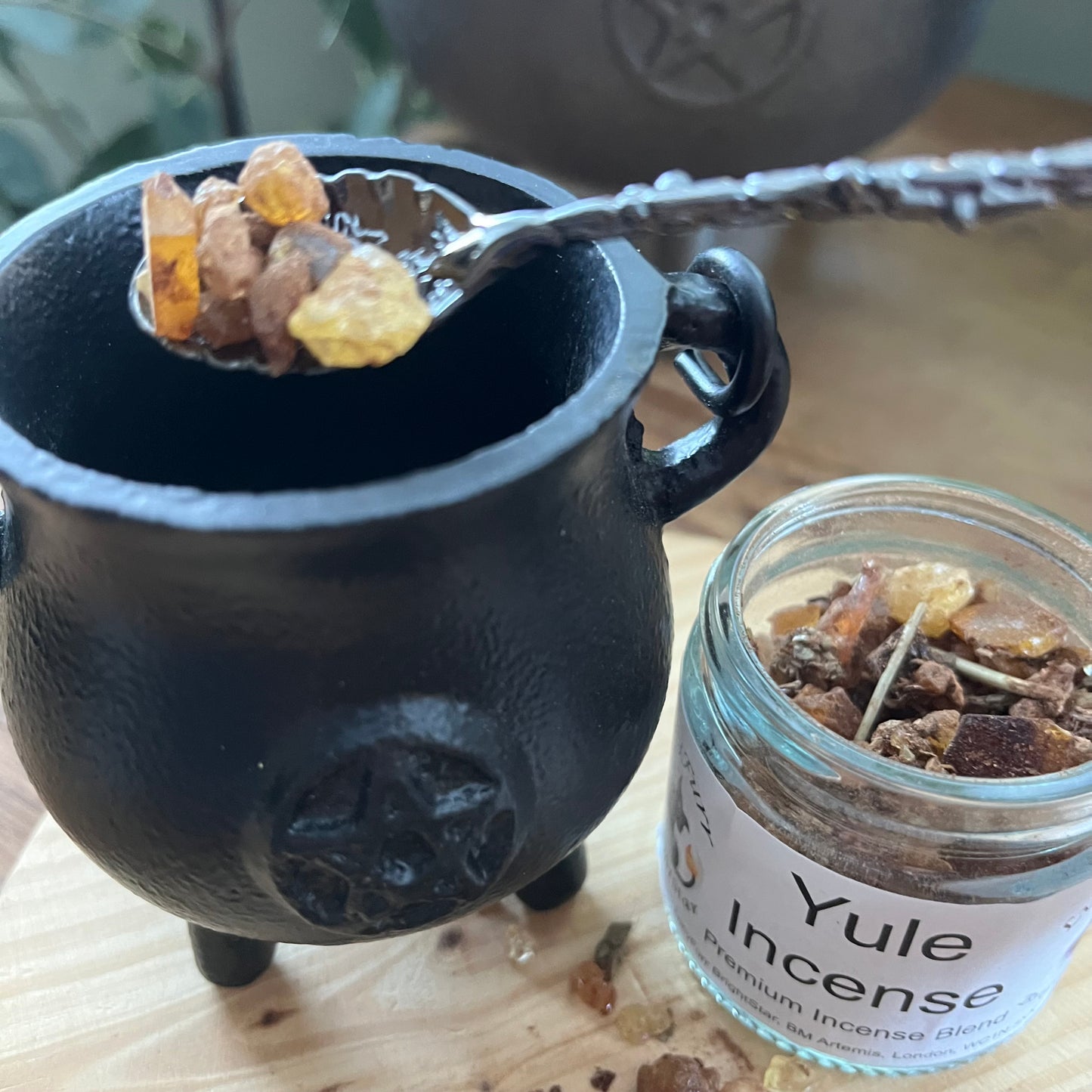 Black cauldron with Yule incense and a jar of Yule incense on a wooden surface.