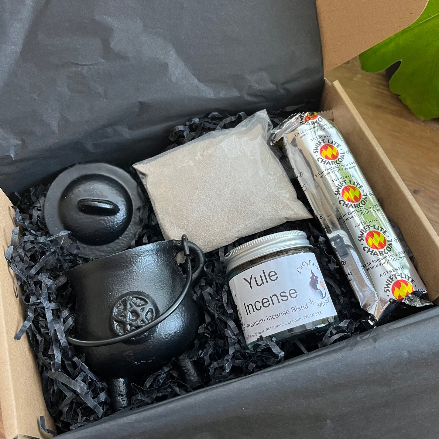 Gift Box containing Yule Incense, a black cauldron and other items on a wooden surface.