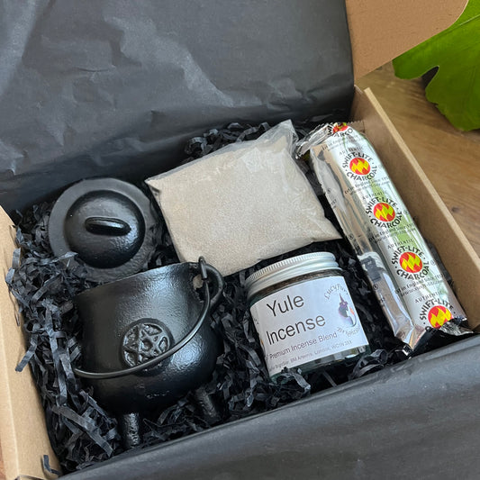 Gift Box containing Yule Incense, a black cauldron and other items on a wooden surface.