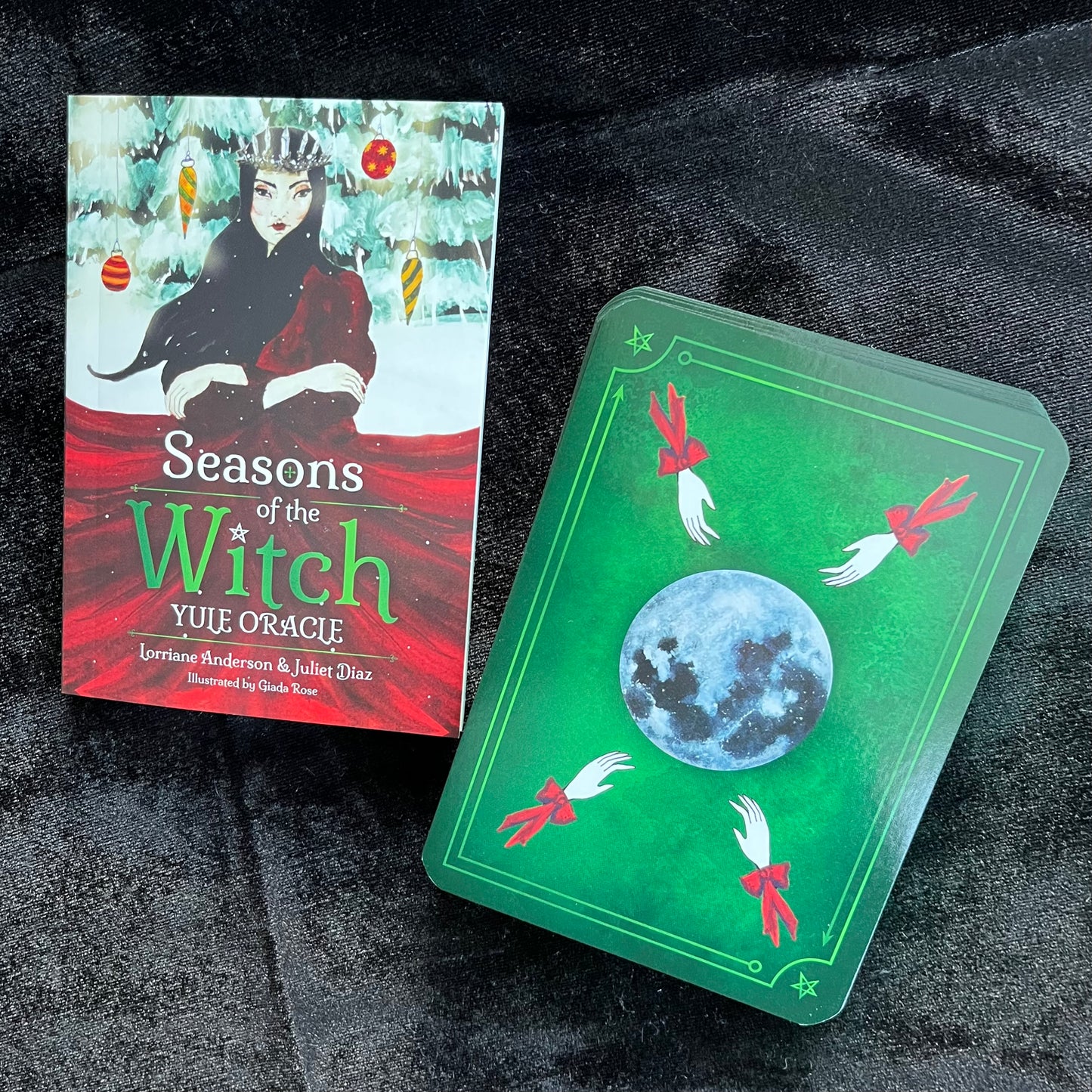 Book titled 'Seasons of the Witch Yule Oracle' with a green card featuring a moon and wiccan symbols on a dark textured background.