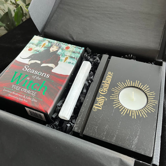 Box containing 'Seasons of the Witch' oracle cards, a selenite stick, and 'Daily Guidance' Tarot stand with a candle on top.