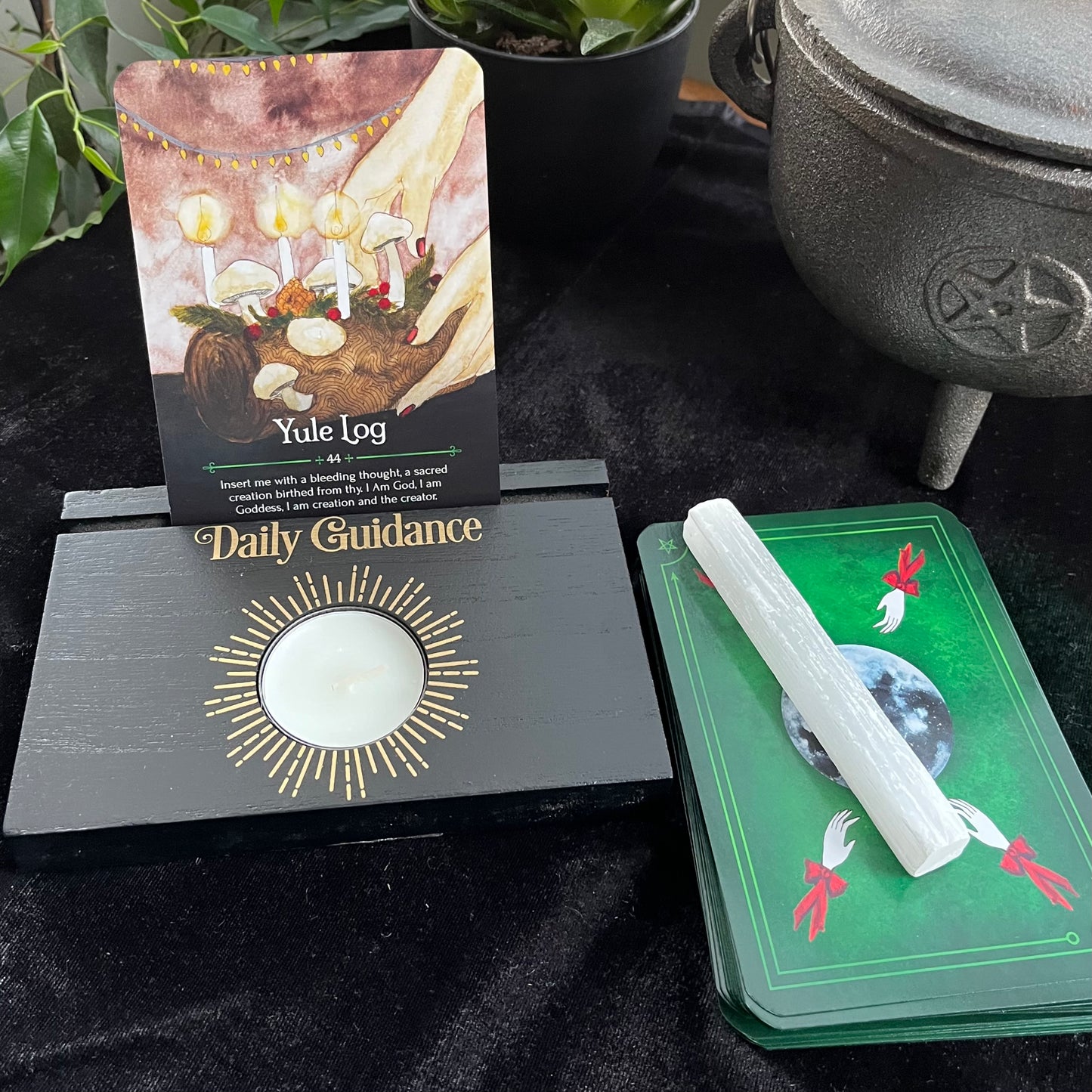 Witchcraft items including a Yule log card, Daily Guidance card, and a green card with a selenite stick on a black surface.